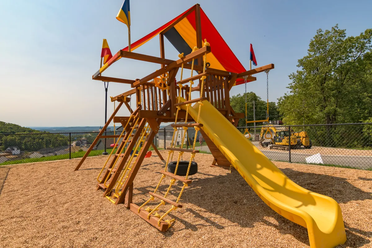 This cheerful exterior captures a vibrant playground complete with a slide, climbing wall, flags, and open space for running and playing. The setting is designed for children’s enjoyment, ideal for family gatherings and creating lasting memories.