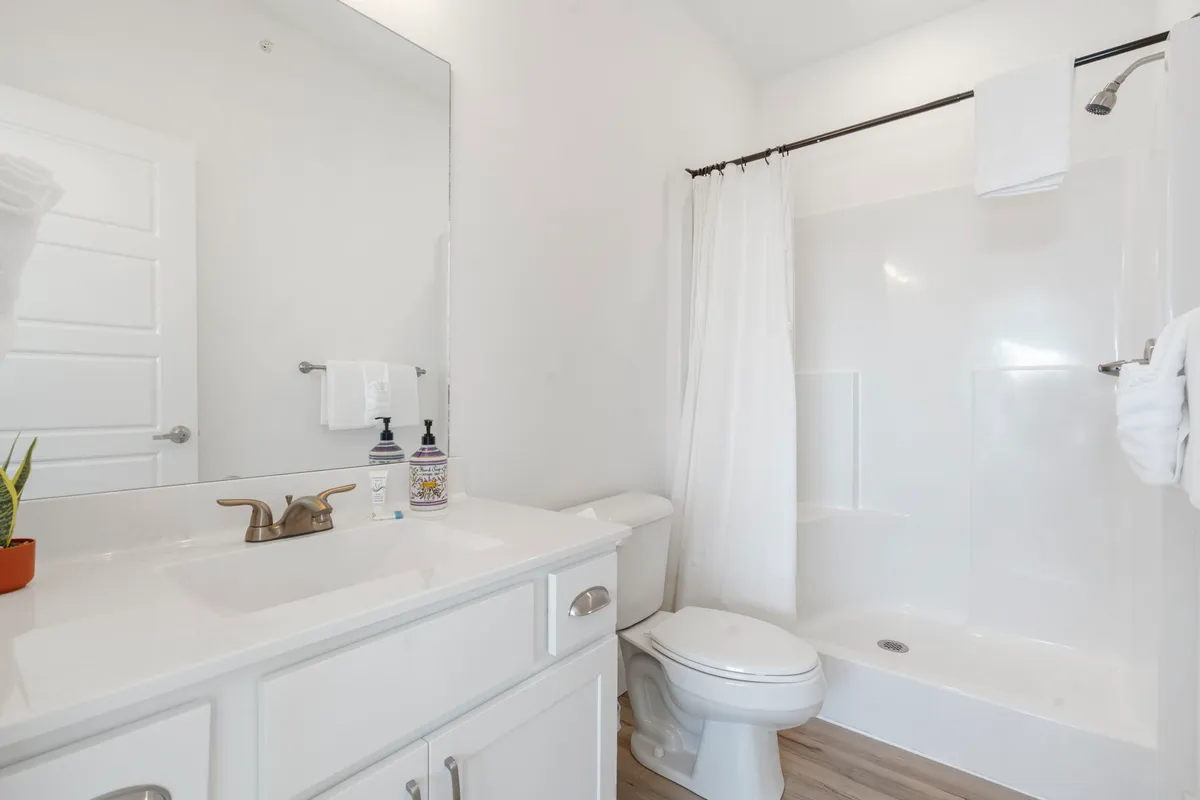 A clean, modern bathroom with a vanity, large mirror, shower, and toilet. The space is bright and fresh, providing a sense of convenience and comfort for guests seeking privacy or shared usage.