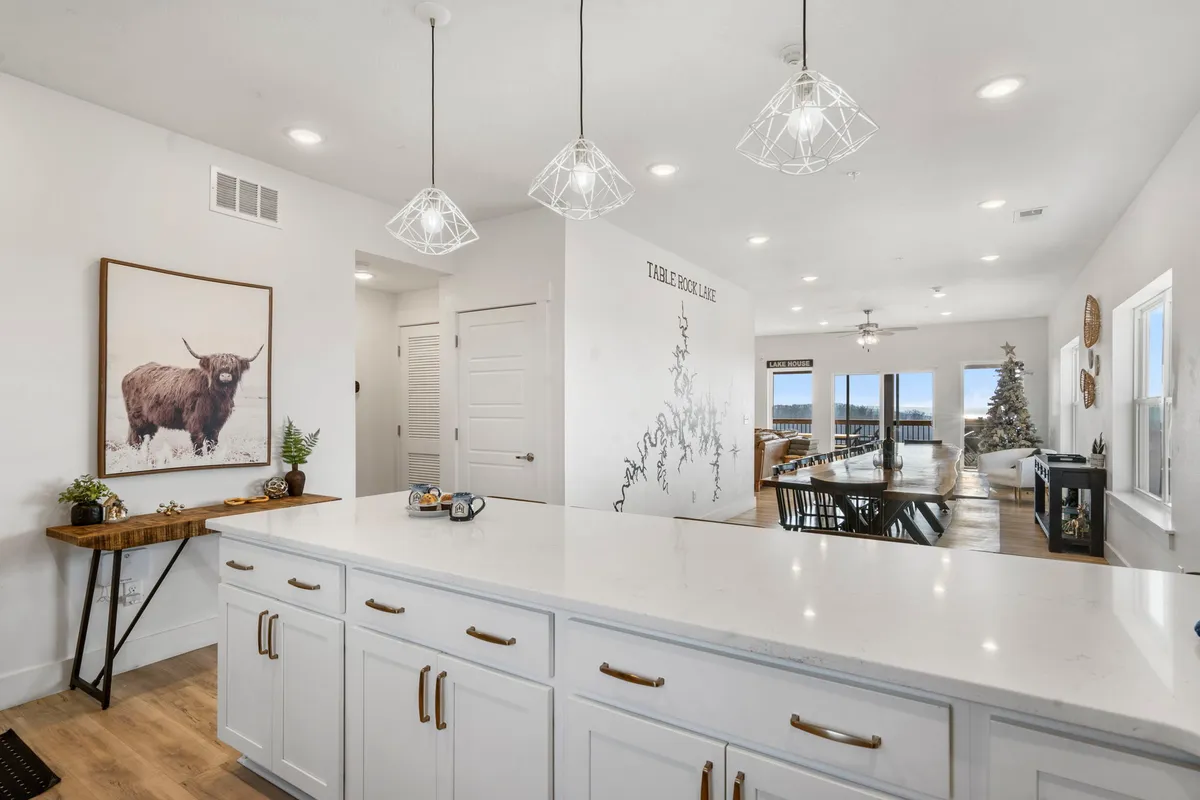 A spacious open-concept kitchen flows seamlessly into a dining area with a large kitchen island, decorative pendant lights, festive wall art, and a dining table set near a Christmas tree. The setting exudes warmth and togetherness, showcasing both the kitchen and dining spaces as central gathering points.