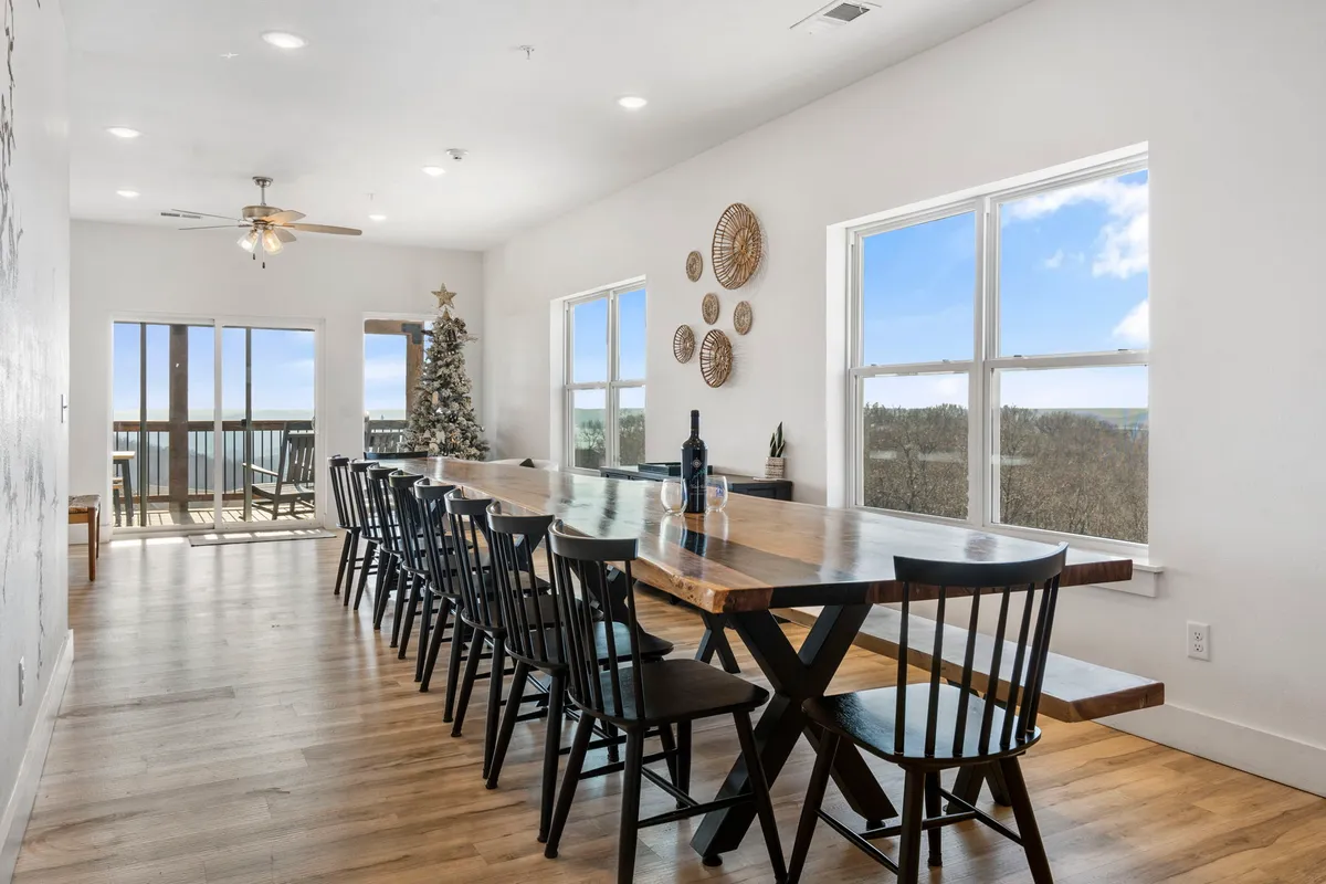 A large, live-edge wooden dining table is surrounded by black chairs, with decorative wall hangings and a Christmas tree adding a festive touch. Large windows let in natural light and offer views to the outside, making the space feel bright and welcoming.