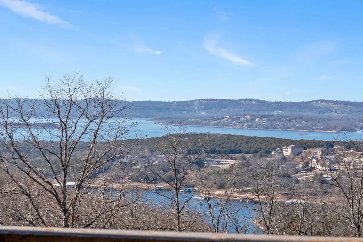 A tranquil lake view framed by gently rolling hills and lush trees. The calm water reflects the sky, evoking the natural beauty of the Ozarks and offering a glimpse of the region's outdoor adventure opportunities like boating, fishing, and hiking.