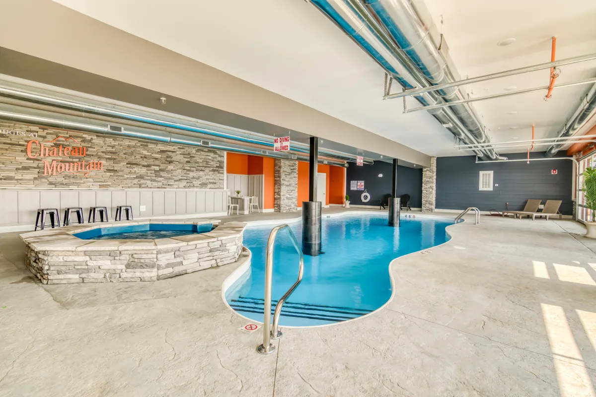 This inviting interior image features a bright indoor pool and hot tub area, with relaxing lounge chairs and the 'Chateau Mountain' sign in view. The tranquil space is designed for recreation and relaxation, regardless of the weather outside.