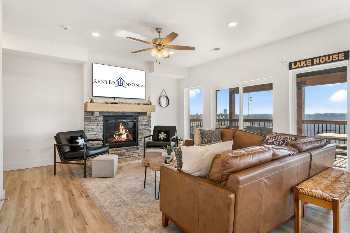 A cozy living area features a fireplace as the focal point, comfortable seating arranged to encourage conversation, and large windows overlooking the lake. A TV is mounted above the fireplace, blending relaxation and entertainment in a welcoming space.