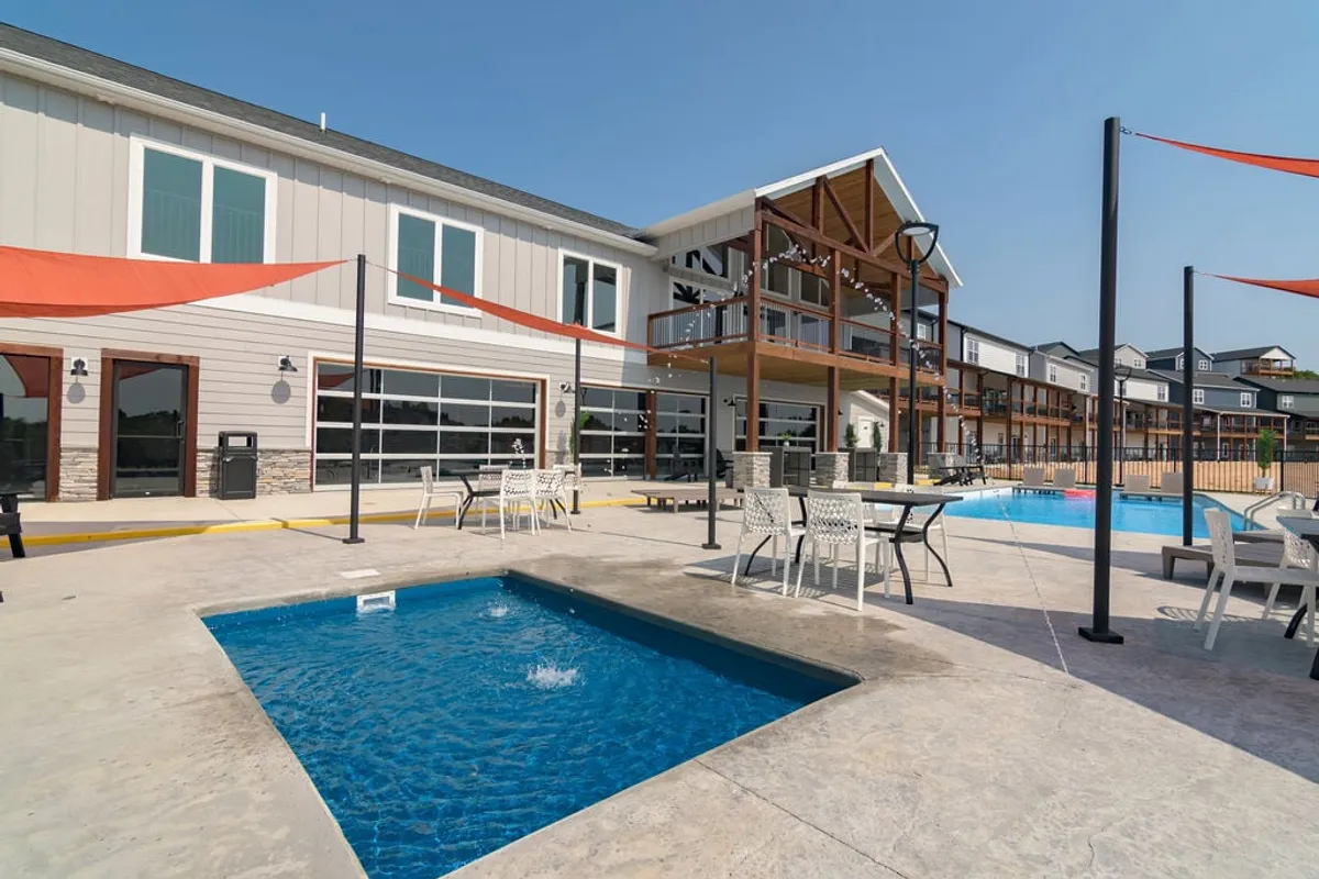 A vibrant exterior space featuring a sparkling swimming pool, inviting hot tub, ample outdoor seating, and modern architectural details. The canopies provide shaded areas for lounging, and the design encourages group activities and relaxation. The scene is set during daylight, suggesting opportunities for both sunbathing and socializing.