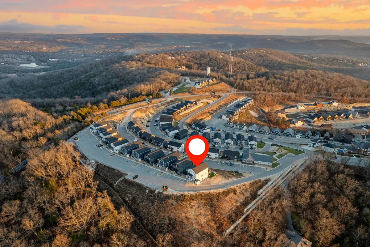 A neighborhood-wide aerial view showcasing the highlighted property and surrounding homes, winding road, and a picturesque sunset sky. The scene captures a sense of community and the potential for exploring the area with friends or family.